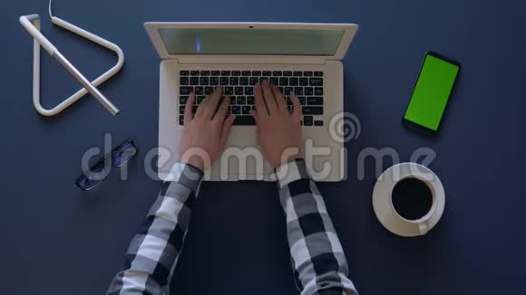穿灰色衬衫的女孩坐在桌子旁喝咖啡时正在笔记本电脑上打字电话和眼镜在上面视频的预览图