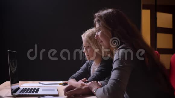 一位年轻的高加索女人和她可爱的小女儿在笔记本电脑上看电影的特写镜头视频的预览图