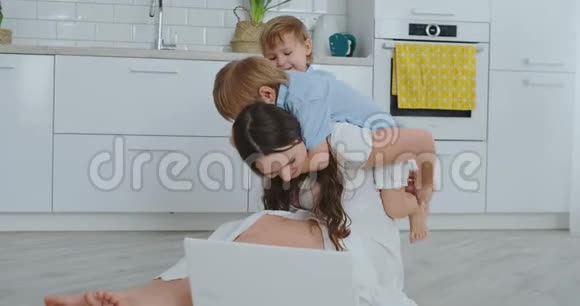 妈妈和两个孩子玩坐在地板上拥抱和玩一个幸福的家庭看完手提电脑后的游戏视频的预览图