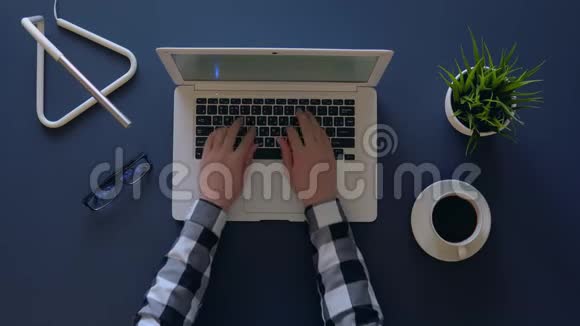 穿灰色衬衫的创意女孩正坐在桌子旁喝咖啡时在笔记本电脑上打字就在附近视频的预览图