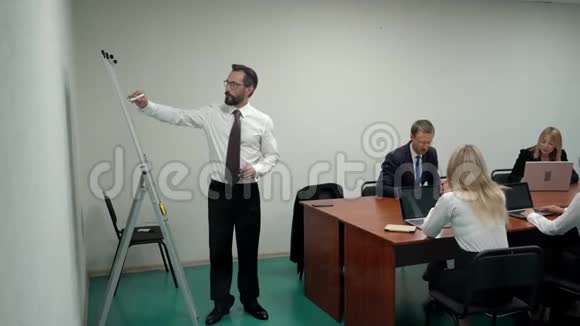 一个商人在会议室里讨论白板上的挂图然后站在办公室里给工作组视频的预览图