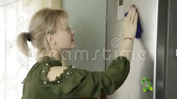 年轻漂亮的女孩用洗涤剂清洗厨房冰箱女佣在厨房擦冰箱视频的预览图