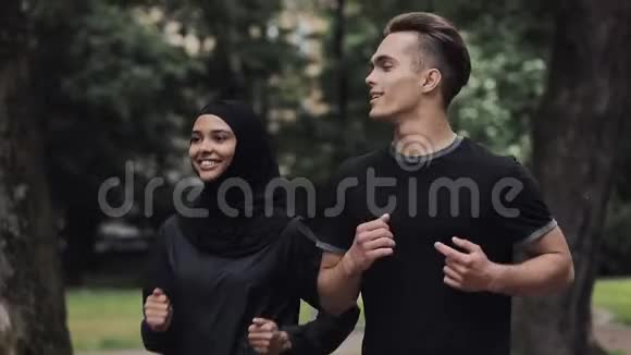 年轻的高加索人和穿着Hijab的穆斯林女人看起来兴奋和放松微笑和聊天在公园里奔跑视频的预览图