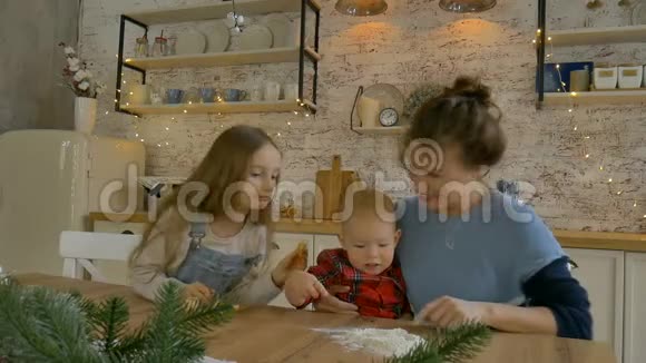 年轻的卷曲妈妈和她的儿子和女儿正在家中烹饪圣诞饼干用圣诞装饰视频的预览图