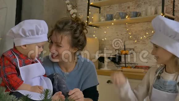 年轻的卷曲妈妈和她的儿子和女儿正在家中烹饪圣诞饼干用圣诞装饰视频的预览图