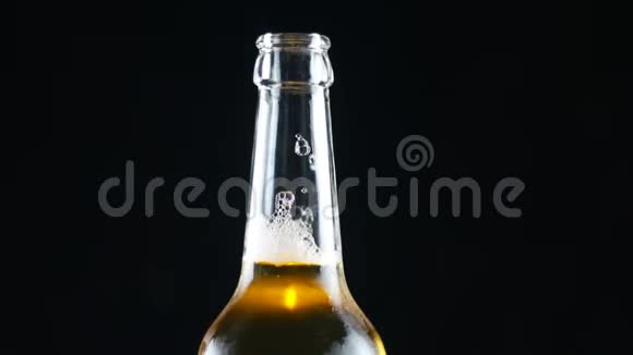 开着的瓶子里的冷啤酒在黑色背景上旋转明亮的灯光视频的预览图