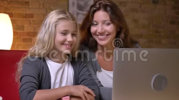 年轻母亲和她漂亮的小女儿一起使用笔记本电脑的特写镜头兴奋地交谈着视频的预览图