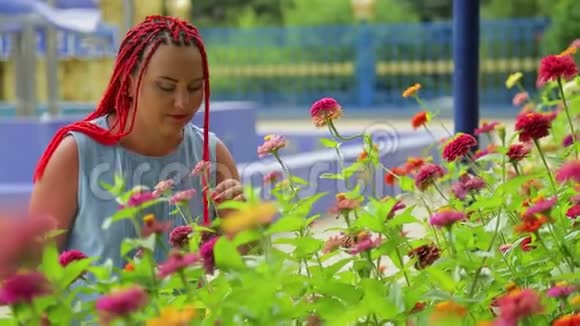 红头发的女人欣赏公园里美丽的花朵视频的预览图