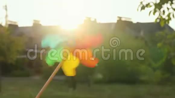 塑料彩虹风车在模糊的房子和日落的背景上旋转郊区概念视频的预览图