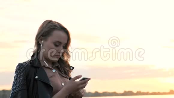 迷人的女孩在耳机使用智能手机自然行走听音乐和浏览智能手机视频的预览图