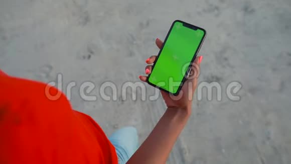 POV女性手握智能手机在沙滩上行走的空白绿色屏幕视频的预览图