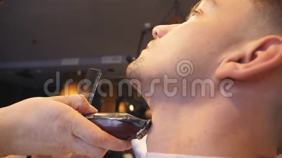 理发店用电动剃须刀修剪年轻顾客胡须的专业理发师男性手武器视频的预览图