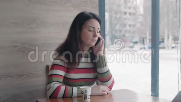 近景穿着针织毛衣的漂亮女人打电话坐在冬季咖啡厅喝咖啡视频的预览图
