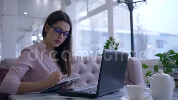 电子学习技术女孩在笔记本电脑设备上在线交流并在咖啡馆的桌子上展示带有笔记的记事本视频的预览图