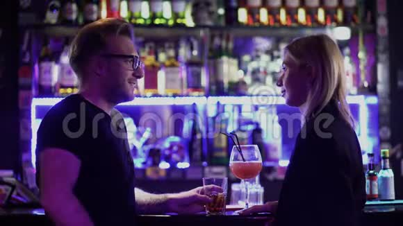 成人夫妇在酒吧柜台喝鸡尾酒戴眼镜的男人和金发女人在迪斯科舞厅聊天玩得开心视频的预览图