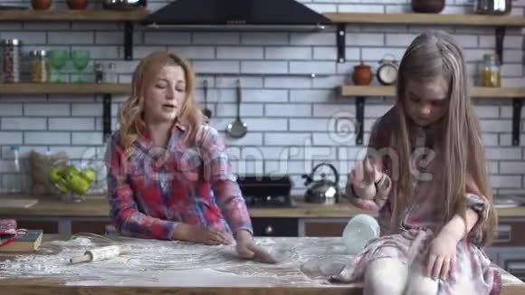 年轻的金发母亲浑身脏乱穿着面粉女儿在基顿桌上玩面粉视频的预览图