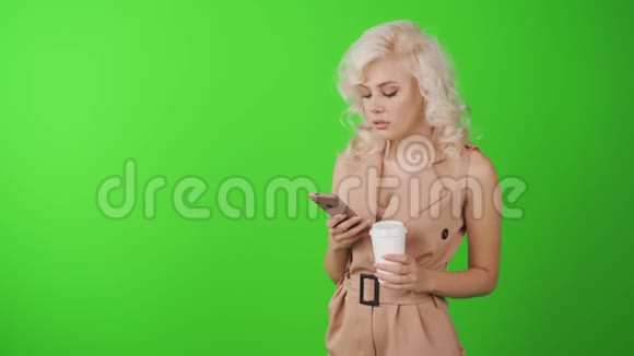 一个微笑的休闲女人拿着智能手机在绿色背景上和一杯咖啡的肖像视频的预览图