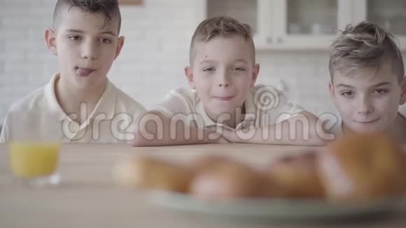 三个男孩看着盘子桌上站着美味的小馅饼孩子们都饿了概念视频的预览图
