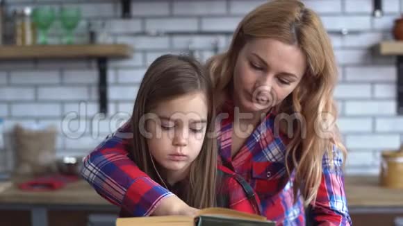 妈妈和女儿坐在厨房的桌子上妈妈为她的小女孩读了一本书视频的预览图