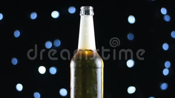 开着瓶子的啤酒在黑色背景上旋转明亮的灯光视频的预览图