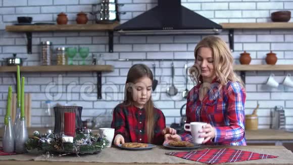 妈妈和穿格子衬衫的小女儿在厨房吃早餐一起吃饼干和喝茶视频的预览图