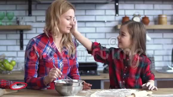 快乐的母亲和女儿在厨房玩耍小女孩在妈妈脸上涂面粉视频的预览图