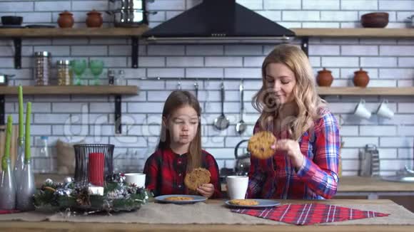 母亲和女儿坐在厨房的桌子上吃着带咖啡的饼干视频的预览图