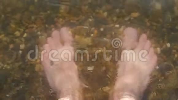 一个人光着脚在海里的鹅卵石海滩上水冲走了一个人的脚视频的预览图