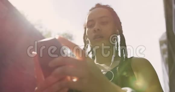 城市中使用手机的年轻非裔美国妇女的低角度视角视频的预览图
