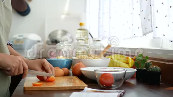 4K镜头女人她的手切片番茄与食谱书打开在前台准备食材烹饪在厨房柜台视频的预览图