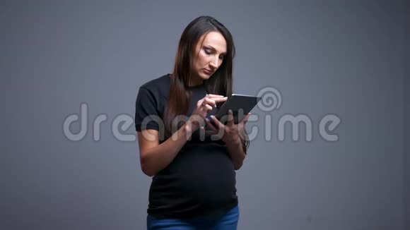 在平板电脑上打字的年轻白种人孕妇的特写照片看着镜头微笑视频的预览图