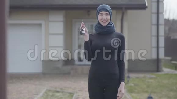 独立微笑的年轻穆斯林妇女手持和挥舞着戴着传统头巾的汽车钥匙的画像视频的预览图