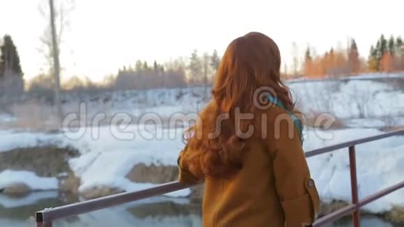 一位年轻的红发女子在日出时沿着桥过一条小河视频的预览图