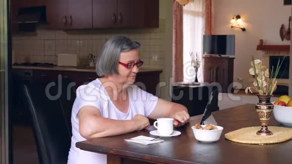 带咖啡的老妇人在家使用数码平板电脑视频的预览图