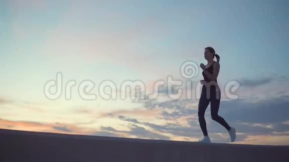 年轻女子正在奔跑在日落时分身影映衬着多云的天空视频的预览图