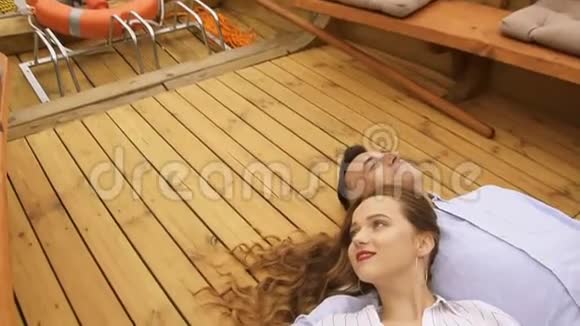 一对年轻夫妇在夏天躺在移动的船甲板上穿着白色深色长发的女孩在温暖的小船上旅行视频的预览图