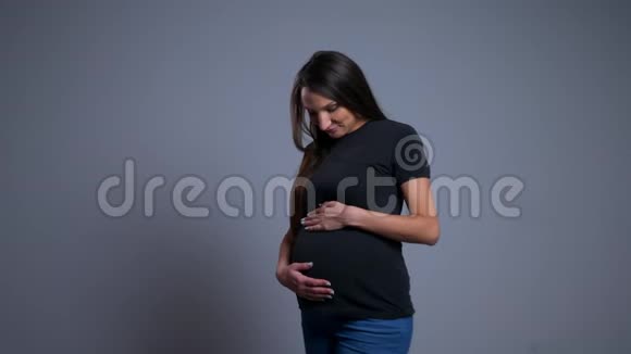 怀孕的年轻白人妇女抱着并用手掌捂住腹部微笑着给婴儿爱的特写照片视频的预览图