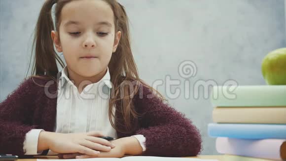 一个漂亮的女学生在灰色背景下坐在桌子旁在这段时间里拿着笔视频的预览图