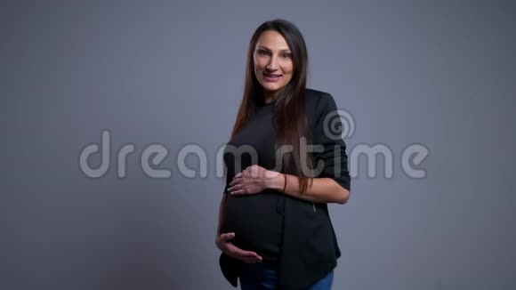 年轻快乐的白种人孕妇的特写镜头双手抓着她的腹部看着摄像机和视频的预览图