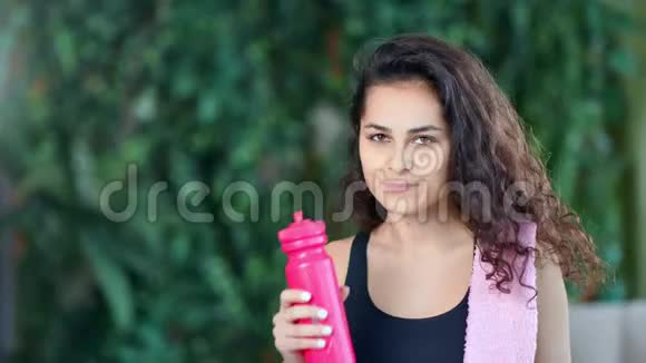 中等身材的漂亮的健身女孩在训练后从瓶子里喝水视频的预览图