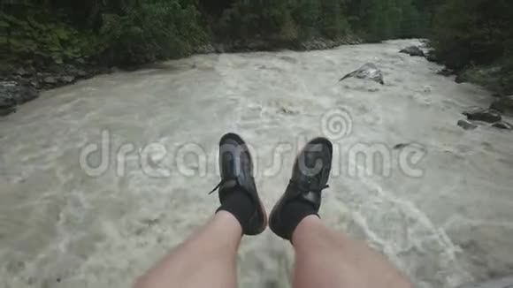 一个人坐在一座木桥上两条腿悬在地上一条湍急的山河流淌山地旅行视频的预览图