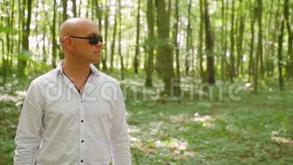 一个戴太阳镜的秃头穿过树林的肖像绿树夏天森林大自然中弹视频的预览图