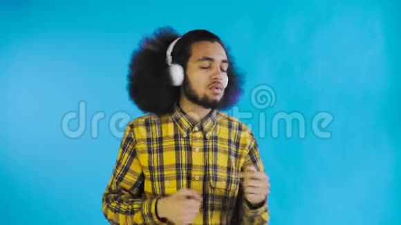 积极的非裔美国人听音乐在他的耳机蓝色背景情感概念视频的预览图