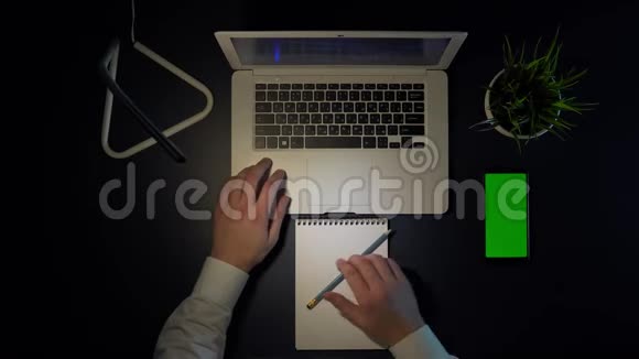 穿着白色衬衫的男人坐在桌子旁用笔记本电脑和电话视频的预览图