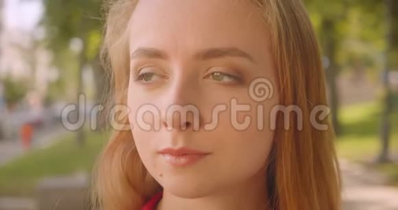 一位年轻可爱的白种人女性金发碧眼看着站在公园户外的摄像机视频的预览图
