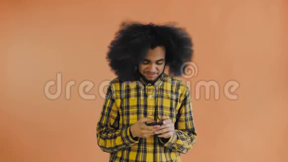 美国黑人卷发男子在橙色背景下的智能手机上聊天的肖像情感概念视频的预览图