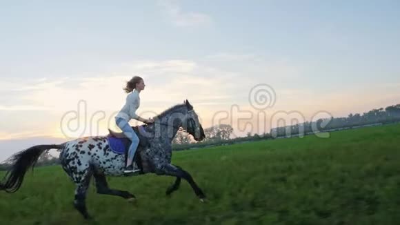 日落时骑在草地上的小女孩的超慢动作视频的预览图