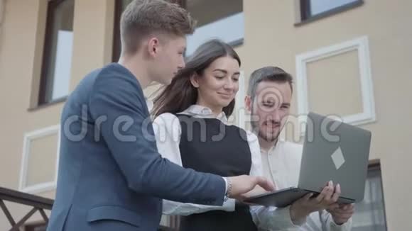 肖像年轻女子和两名男子在正式穿着讨论项目的笔记本电脑在露台上业务关系视频的预览图
