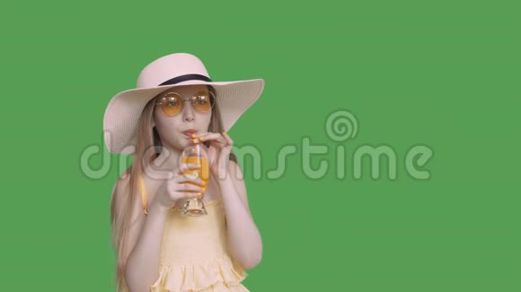 少女在透明的绿色背景下用吸管喝橙汁戴黄色眼镜的年轻女孩视频的预览图