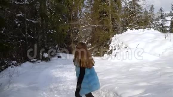 年轻漂亮的女孩跑在一片白雪皑皑的冬林里她既快乐又开朗漂亮的金发美女慢动作视频的预览图